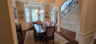 Dining area with a chandelier, coffered ceiling, dark wood-style flooring, a decorative wall, and ornamental molding