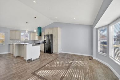 Kitchen with cream cabinetry, black fridge, light wood-style floors, vaulted ceiling, and decorative light fixtures