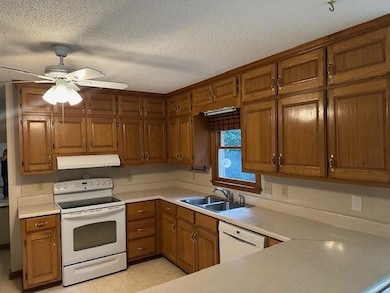 Kitchen featuring white appliances, a sink, under cabinet range hood, brown cabinets, and light countertops