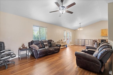 Living room featuring vaulted ceiling, wood finished floors, plenty of natural light, ceiling fan, and a chandelier