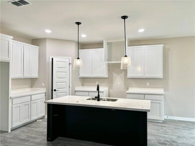 Kitchen featuring white cabinets, a center island with sink, and decorative light fixtures