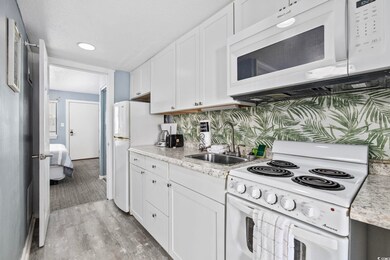 Kitchen featuring white appliances, a sink, white cabinetry, light wood-type flooring, and light stone countertops