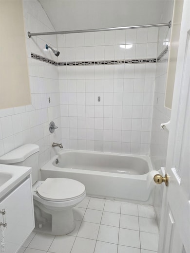 Bathroom with light tile patterned floors, bathtub / shower combination, tile walls, and vanity