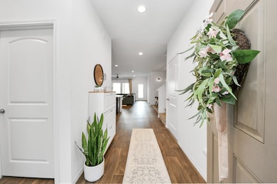 Step through the front door and into a bright, welcoming entryway adorned with warm wooden floors, cheerful décor, and a charming floral wreath that sets the tone for the rest of the home. This stylish space flows seamlessly into an open-concept living area, where modern elegance meets everyday comfort—perfect for both relaxing and entertaining.

