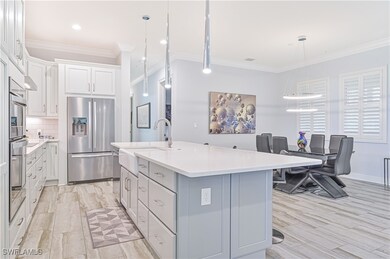 Kitchen with stainless steel refrigerator with ice dispenser, a center island with sink, hanging light fixtures, and sink