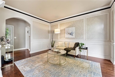 Living area featuring arched walkways, a decorative wall, wood finished floors, and crown molding