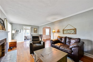 Living room with crown molding, light wood-type flooring, arched walkways, a fireplace, and a textured ceiling