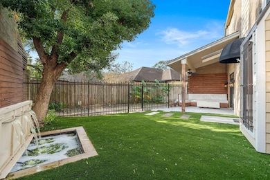This front yard features a cozy seating area with a covered patio, artificial turf for easy maintenance, a charming water feature, and a tree providing shade. It's enclosed with a fence for privacy.