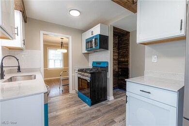 Kitchen with gas range, light stone countertops, light wood-style flooring, white cabinets, and decorative backsplash