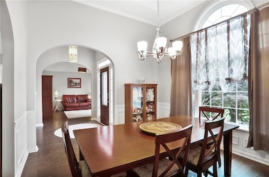 Dining area featuring tall tray ceiling, new windows, a chandelier, wood flooring, arched walkways, and crown molding