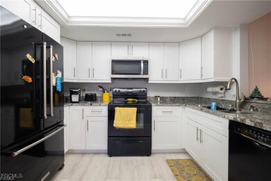 Kitchen featuring black appliances, white cabinetry, light stone counters, and light wood-type flooring