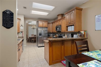 Kitchen featuring appliances with stainless steel finishes, a peninsula, arched walkways, light stone countertops, and a chandelier