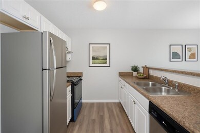 (Virtually Staged) Kitchen featuring appliances with stainless steel finishes, a sink, wood finished floors, white cabinetry, and baseboards