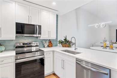 Kitchen with recessed lighting, a sink, stainless steel appliances, decorative backsplash, and white cabinetry