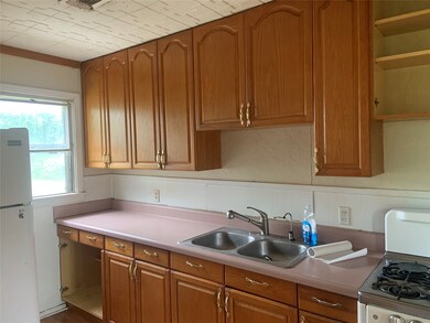 Kitchen featuring a sink, freestanding refrigerator, gas range, brown cabinetry, and light countertops