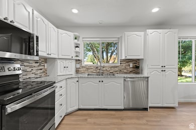 Kitchen featuring appliances with stainless steel finishes, open shelves, light stone countertops, white cabinets, and light wood-style flooring