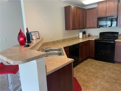 Kitchen with black appliances, a sink, a peninsula, light countertops, and a kitchen breakfast bar