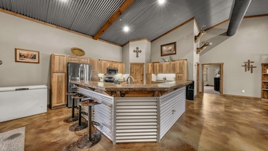 Kitchen featuring a kitchen breakfast bar, high vaulted ceiling, concrete floors, appliances with stainless steel finishes, and a spacious island