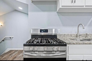 Kitchen featuring stainless steel range with gas stovetop, white cabinetry, light stone countertops, and wood finished floors
