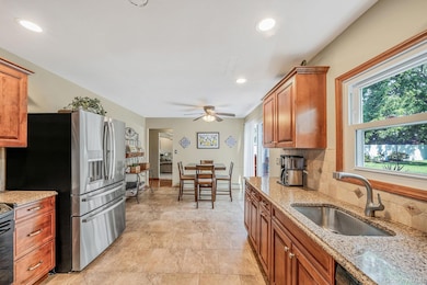 Kitchen with light stone countertops, stainless steel fridge, recessed lighting, brown cabinets, and tasteful backsplash