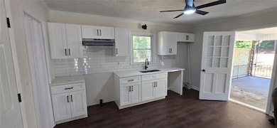 Kitchen featuring white cabinets, decorative backsplash, crown molding, dark wood-style flooring, and under cabinet range hood