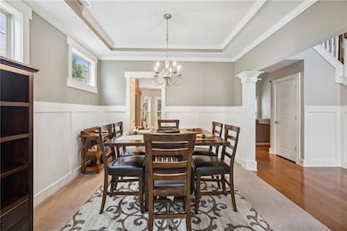 Dining space with a decorative wall, a chandelier, a raised ceiling, a wainscoted wall, and ornamental molding