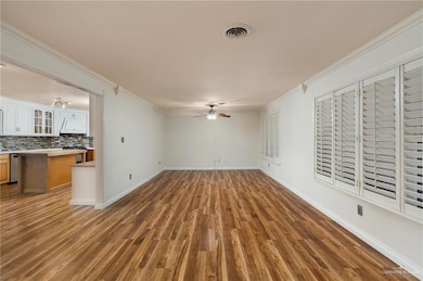 Unfurnished living room featuring hardwood / wood-style floors, ceiling fan, and ornamental molding