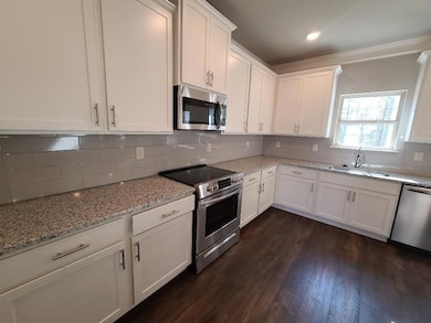 Kitchen featuring appliances with stainless steel finishes, white cabinets, decorative backsplash, light stone counters, and ornamental molding