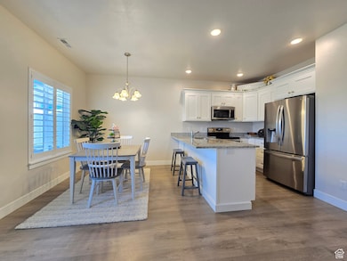 Kitchen featuring stainless steel appliances, light stone countertops, white cabinetry, dark wood-type flooring, and a breakfast bar area