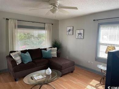 Living area featuring a textured ceiling, light wood-style flooring, plenty of natural light, and ceiling fan