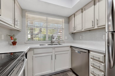 Kitchen featuring appliances with stainless steel finishes, tasteful backsplash, white cabinets, and light stone countertops