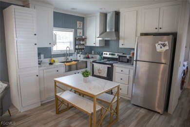Kitchen featuring light countertops, appliances with stainless steel finishes, wall chimney range hood, and white cabinets