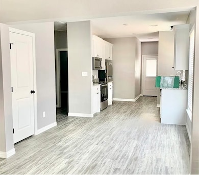 Kitchen with white cabinetry, stainless steel appliances, light wood finished floors, and light stone counters