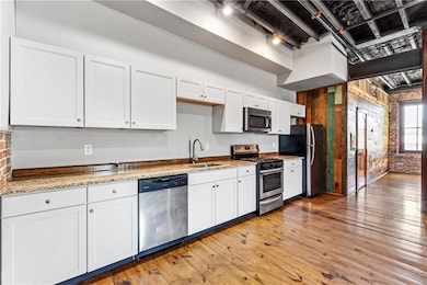 Kitchen featuring stainless steel appliances, brick wall, a sink, white cabinetry, and light wood finished floors