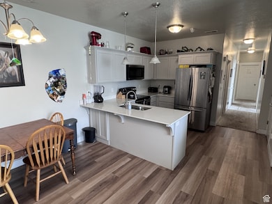 Kitchen featuring stainless steel appliances, a peninsula, hanging light fixtures, dark wood-style floors, and a textured ceiling
