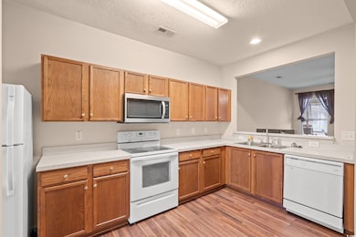 Kitchen with white appliances, light countertops, a textured ceiling, light wood-type flooring, and brown cabinets