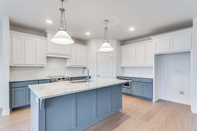 Kitchen featuring hanging light fixtures, a kitchen island with sink, and white cabinets