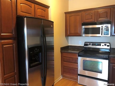 Kitchen featuring appliances with stainless steel finishes, light wood finished floors, dark stone countertops, and brown cabinetry