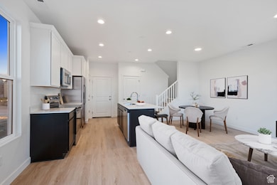 Kitchen featuring a center island with sink, stainless steel appliances, light wood-style floors, dark cabinetry, and open floor plan