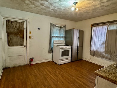 Kitchen with a textured ceiling, white range with electric stovetop, freestanding refrigerator, and dark wood finished floors