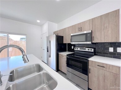 Kitchen featuring appliances with stainless steel finishes, light brown cabinetry, a sink, light countertops, and decorative backsplash