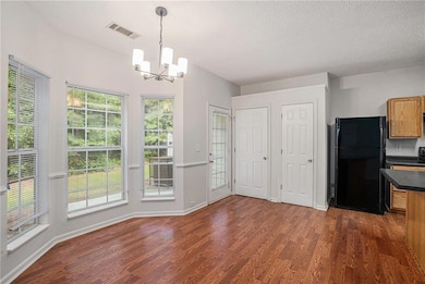 Unfurnished dining area with dark wood-style flooring, a textured ceiling, and a chandelier