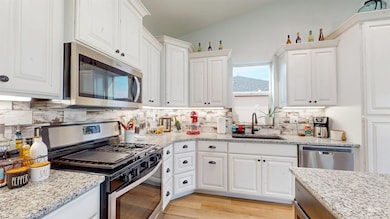 Kitchen with stainless steel appliances, white cabinets, backsplash, light wood-style floors, and light stone counters
