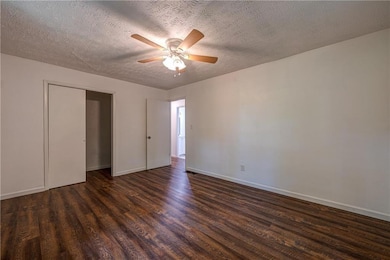 Unfurnished bedroom with dark wood-type flooring, baseboards, a textured ceiling, and a ceiling fan