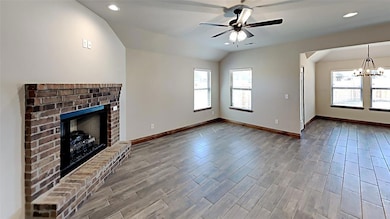 Unfurnished living room featuring plenty of natural light, a fireplace, a chandelier, lofted ceiling, and baseboards