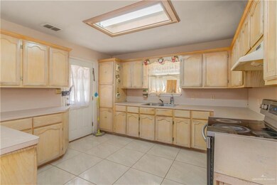 Kitchen with light tile floors, wall chimney exhaust hood, light brown cabinetry, and range with electric stovetop