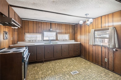 Kitchen with electric stove, wooden walls, light c