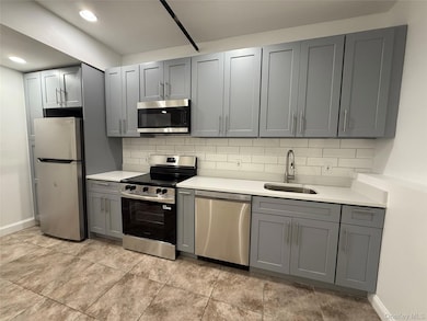 Kitchen with stainless steel appliances, gray cabinetry, backsplash, light countertops, and recessed lighting