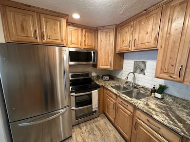 Kitchen featuring stainless steel appliances, dark stone counters, tasteful backsplash, light wood finished floors, and brown cabinets