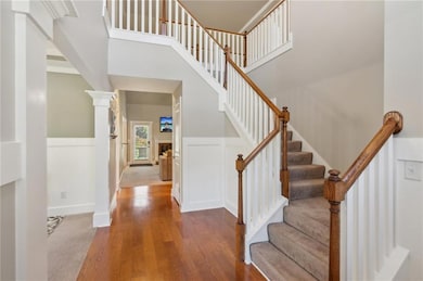 Stairs featuring wood finished floors, a high ceiling, decorative columns, and a wainscoted wall